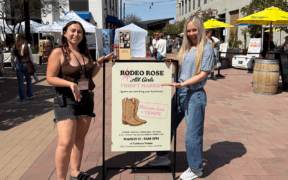 Trinity Roraback and Erin Thorburn standing at Rodeo Rose Market in Tempe Arizona with event sign and vendor tents in background.