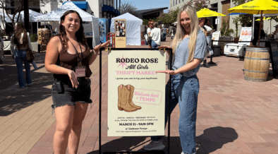 Trinity Roraback and Erin Thorburn standing at Rodeo Rose Market in Tempe Arizona with event sign and vendor tents in background.