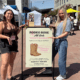 Trinity Roraback and Erin Thorburn standing at Rodeo Rose Market in Tempe Arizona with event sign and vendor tents in background.