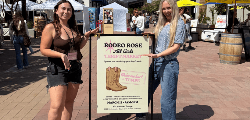 Trinity Roraback and Erin Thorburn standing at Rodeo Rose Market in Tempe Arizona with event sign and vendor tents in background.