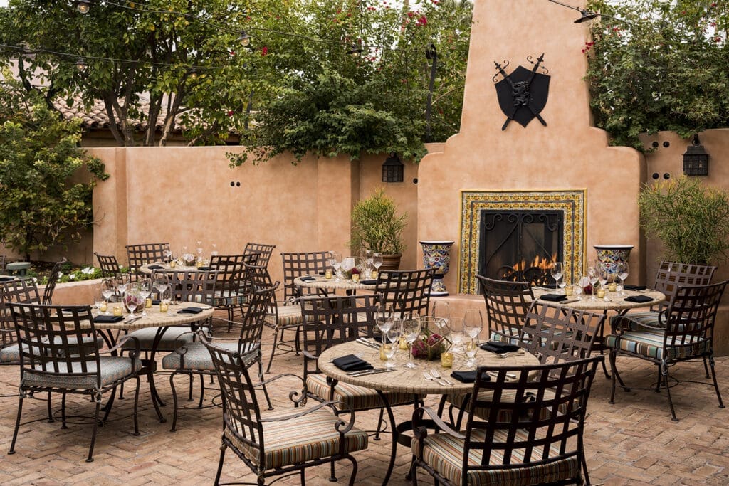 Outdoor patio dining at T. Cook’s at Royal Palms Resort and Spa featuring a fireplace, tiled accents, string lights and an intimate courtyard setting in Phoenix Arizona.