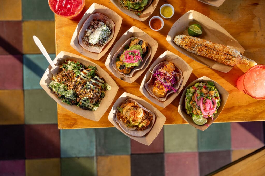A variety of tacos with colorful toppings and elote on table at El Paso restaurant Taconeta.