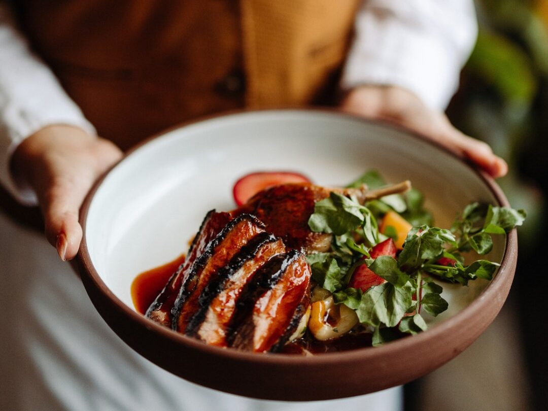 A waiter holds a bowl of steak covered in sauce with a summer fruit and greens salad at The Lodge at Torrey Pines.