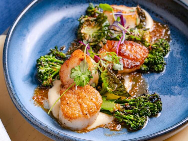 An elevated bowl of scallops with broccolini  and sauce from Westdrift Manhattan Beach.
