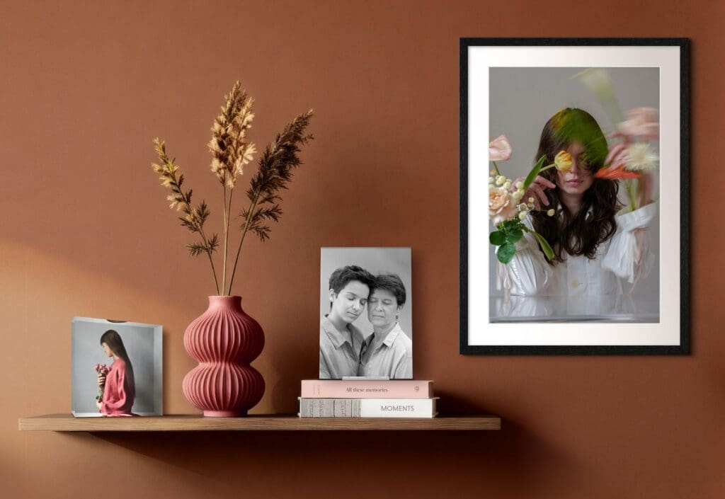 A styled shelf with framed photos, books and decorative objects against a warm-toned wall.