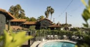 Outdoor pool at Woods Cove Inn in Laguna Beach with palm trees, Spanish-style tile roof and sunny courtyard seating.