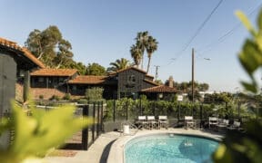 Outdoor pool at Woods Cove Inn in Laguna Beach with palm trees, Spanish-style tile roof and sunny courtyard seating.