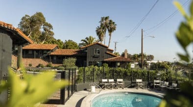 Outdoor pool at Woods Cove Inn in Laguna Beach with palm trees, Spanish-style tile roof and sunny courtyard seating.