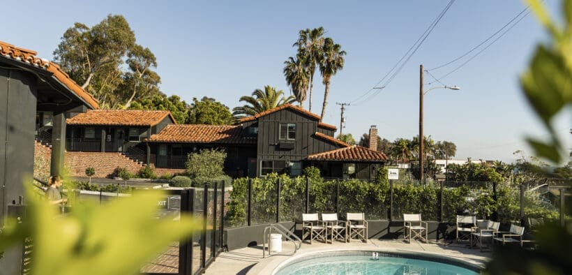 Outdoor pool at Woods Cove Inn in Laguna Beach with palm trees, Spanish-style tile roof and sunny courtyard seating.