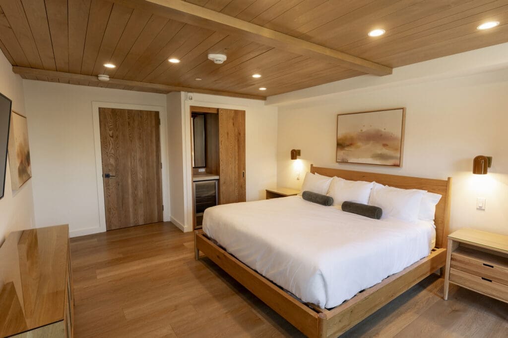 Minimalist guest room at Woods Cove Inn with wood bed frame, white bedding and warm ceiling panels.