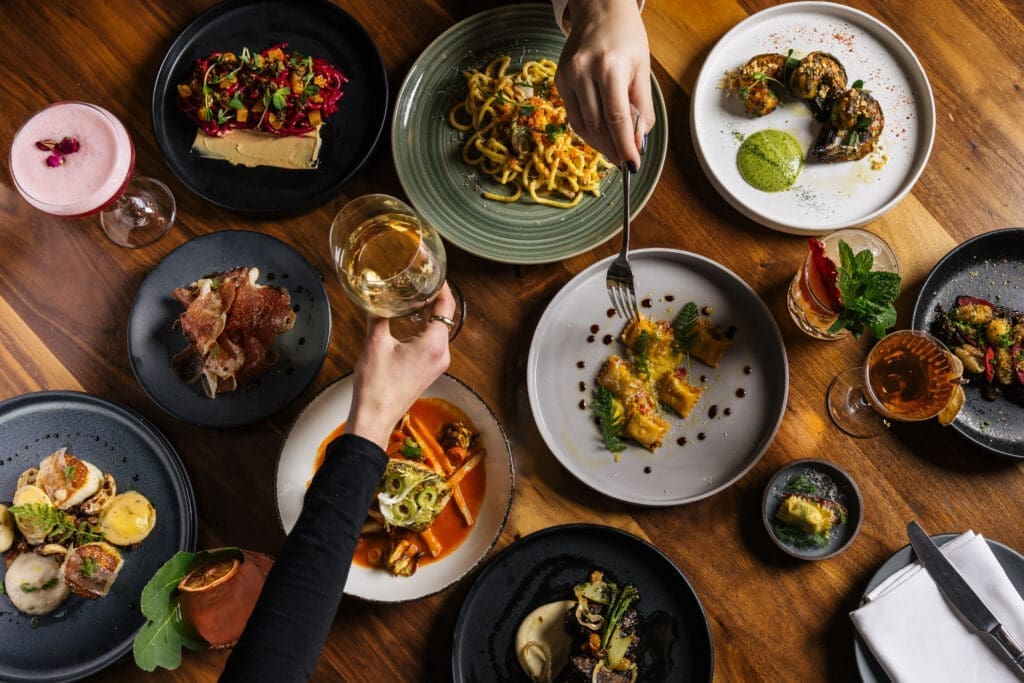 Assorted upscale Italian dishes and cocktails on a wooden table at Fat Ox in Scottsdale.