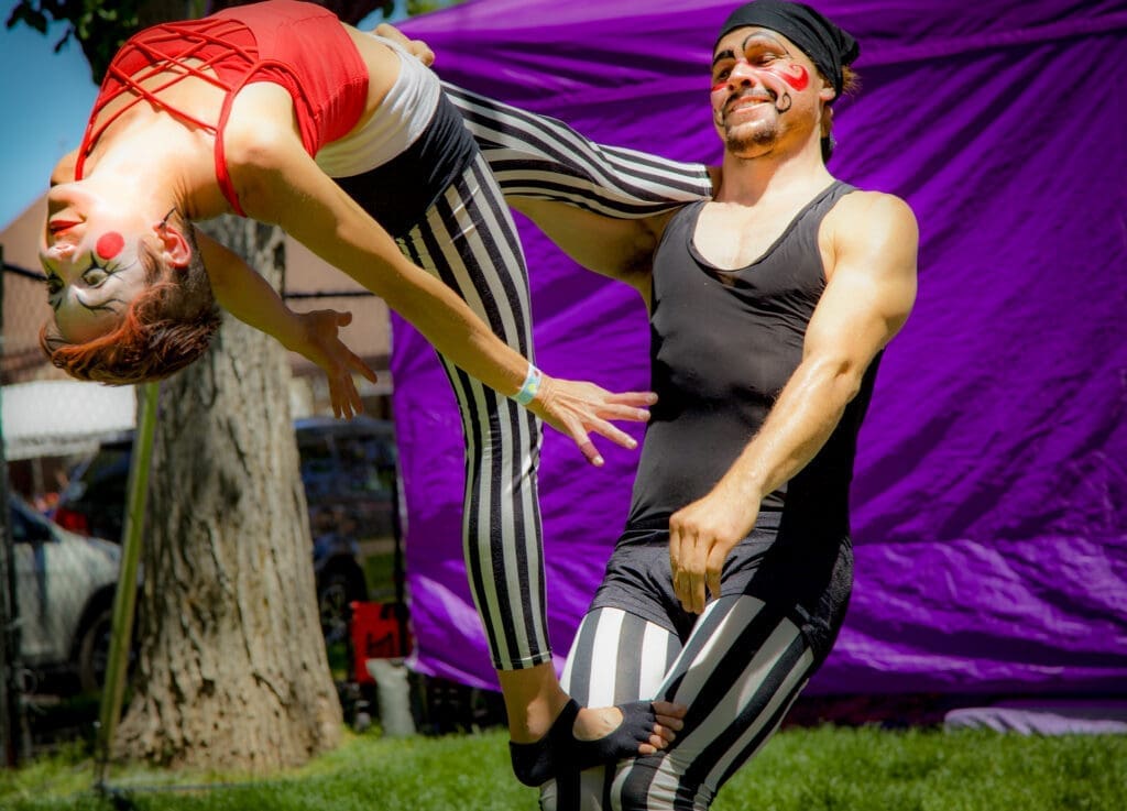 Two performers in striped costumes and face paint performing an acrobatic act outdoors at a Flagstaff festival.