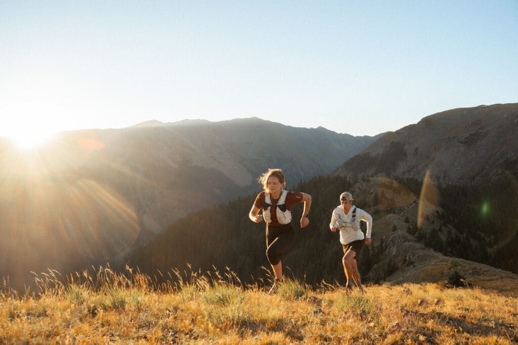 Two trail runners traverse a mountain ridgeline at sunrise in Taos Ski Valley, New Mexico.