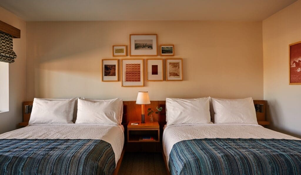 Guest room at Trailborn Grand Canyon featuring two queen beds, warm wood accents, framed artwork and modern desert-inspired decor.