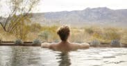 Guest relaxing in an outdoor soaking tub at Miraval Arizona Resort & Spa with desert plants and mountain views in the background.