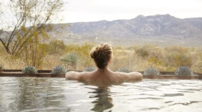 Guest relaxing in an outdoor soaking tub at Miraval Arizona Resort & Spa with desert plants and mountain views in the background.