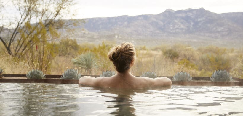Guest relaxing in an outdoor soaking tub at Miraval Arizona Resort & Spa with desert plants and mountain views in the background.