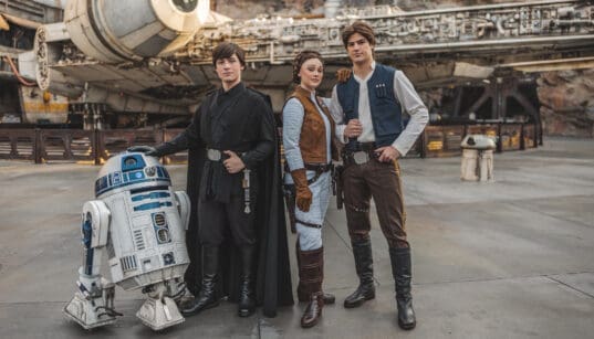 R2D2, Luke Skywalker, Princess Leia, and Han Solo characters stand in front of the Millenieum Falcon at Disneyland Galaxy's Edge.