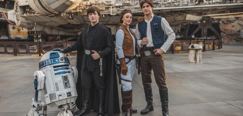 R2D2, Luke Skywalker, Princess Leia, and Han Solo characters stand in front of the Millenieum Falcon at Disneyland Galaxy's Edge.