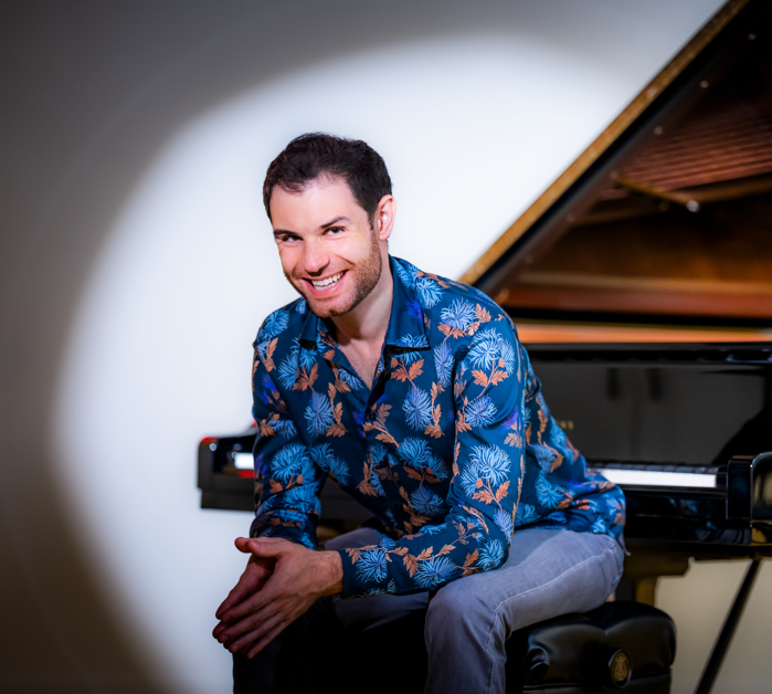 Pianist Drew Petersen smiling while seated beside a grand piano during a portrait session.