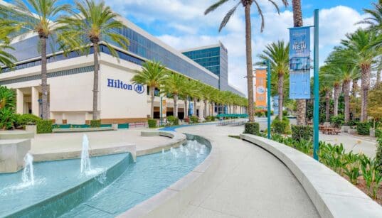 Exterior view of Hilton Anaheim with palm trees, fountain and resort entrance near Disneyland Resort in Anaheim, California.
