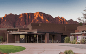 Exterior of the Center for the Arts at Kayenta in Ivins, Utah, with red rock mountains glowing at sunset behind the desert-inspired building.