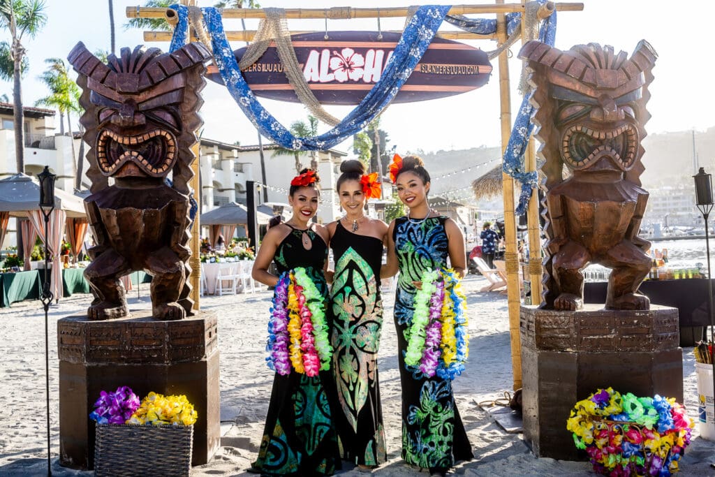 Guests pose beneath tiki statues during Kona Kai San Diego Resort’s annual Lū’au & Island Makeke waterfront summer event in San Diego.