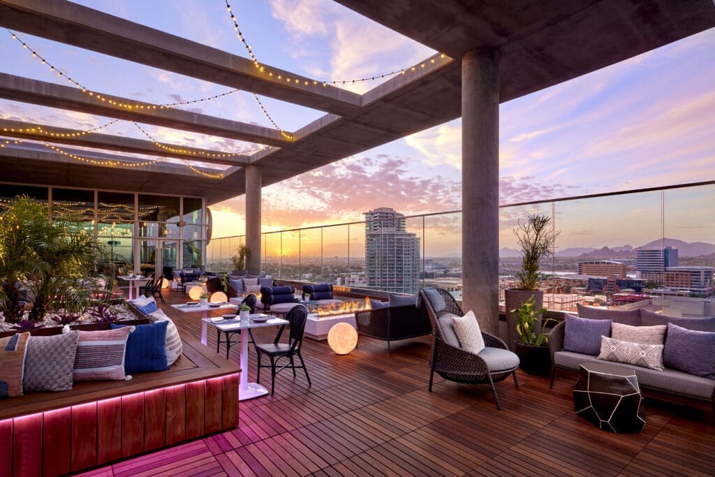 Rooftop patio at Omni Tempe Hotel at ASU featuring lounge seating, string lights and panoramic sunset views overlooking downtown Tempe and the surrounding desert landscape.