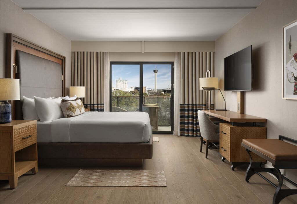 Luxury hotel guest room at Plaza San Antonio Hotel & Spa in San Antonio with king-size bed, furniture and balcony with chairs.