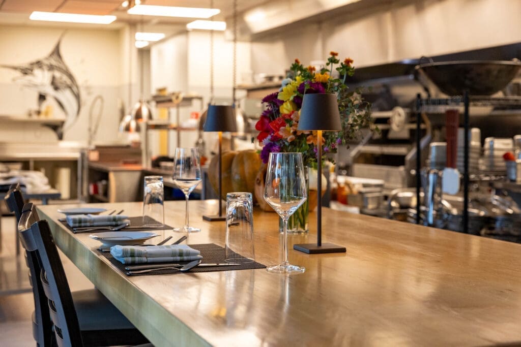 Chef’s counter seating with wine glasses inside Quiessence kitchen at The Farm at South Mountain.