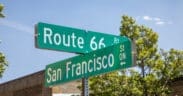 Route 66 and San Francisco Street signs in downtown Flagstaff, beneath a bright blue sky.