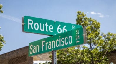 Route 66 and San Francisco Street signs in downtown Flagstaff, beneath a bright blue sky.