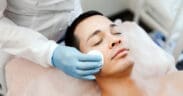 A man receives a professional facial treatment while lying on a spa treatment bed during a skincare appointment.