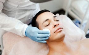 A man receives a professional facial treatment while lying on a spa treatment bed during a skincare appointment.