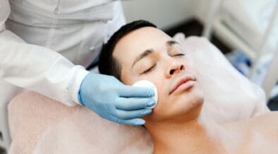 A man receives a professional facial treatment while lying on a spa treatment bed during a skincare appointment.