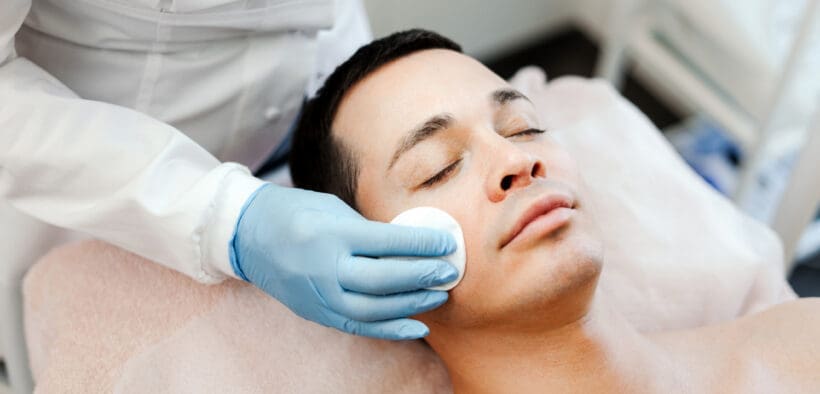 A man receives a professional facial treatment while lying on a spa treatment bed during a skincare appointment.