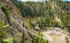 Guests cross a suspension bridge on the Via Ferrata course at Taos Ski Valley during a guided summer mountain adventure.