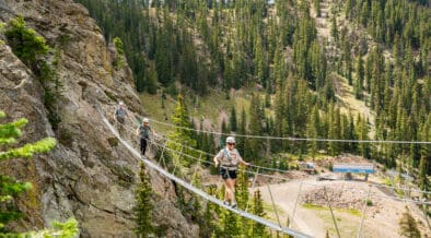 Guests cross a suspension bridge on the Via Ferrata course at Taos Ski Valley during a guided summer mountain adventure.