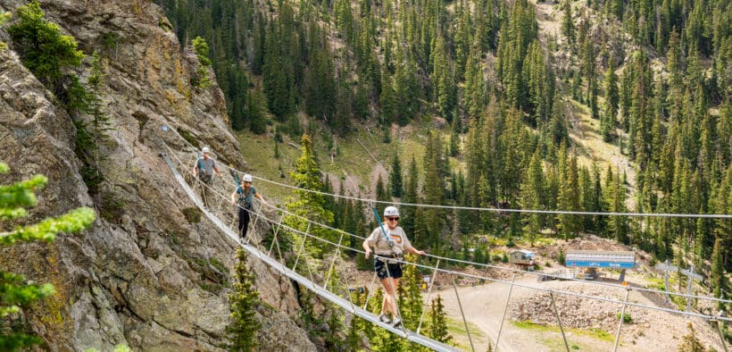Guests cross a suspension bridge on the Via Ferrata course at Taos Ski Valley during a guided summer mountain adventure.