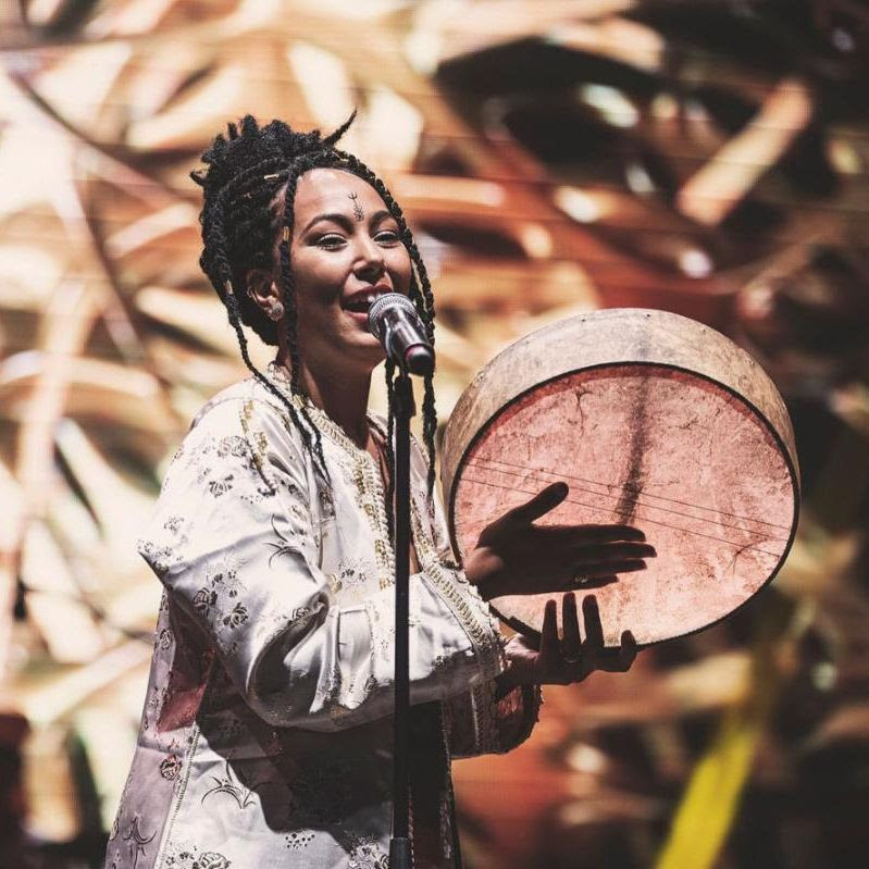 Moroccan artist The Leila singing into a microphone while holding a drum during a live performance.