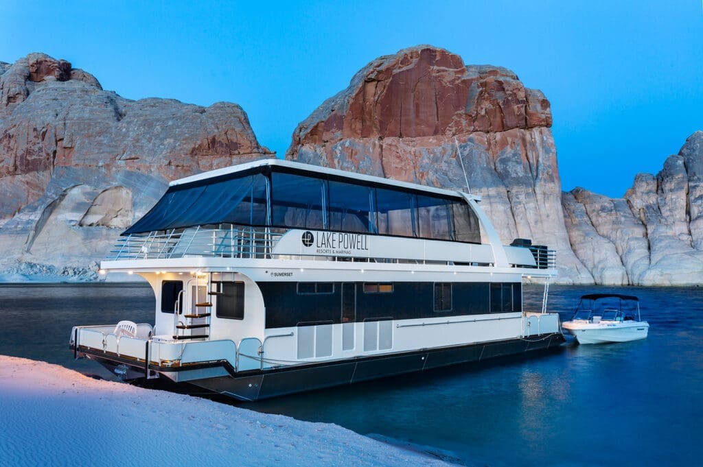 Luxury houseboat from Lake Powell Resorts & Marinas docked on Lake Powell surrounded by towering sandstone canyon walls at dusk.