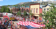 Crowds line Main Street during Breckenridge's Fourth of July celebration with American flags and mountain views in the background.