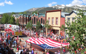 Crowds line Main Street during Breckenridge's Fourth of July celebration with American flags and mountain views in the background.