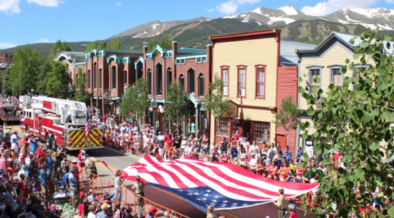 Crowds line Main Street during Breckenridge's Fourth of July celebration with American flags and mountain views in the background.