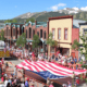 Crowds line Main Street during Breckenridge's Fourth of July celebration with American flags and mountain views in the background.