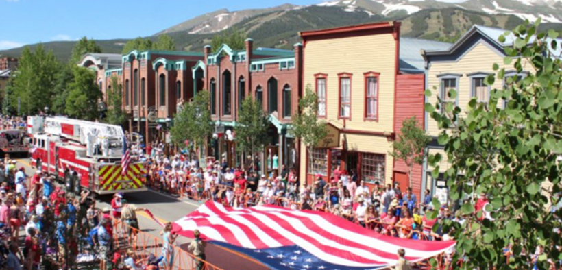 Crowds line Main Street during Breckenridge's Fourth of July celebration with American flags and mountain views in the background.