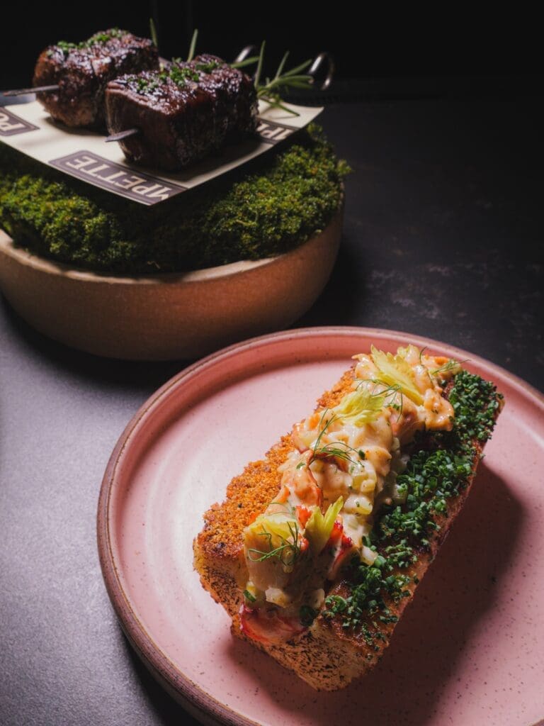 Lobster roll topped with lobster salad and chives alongside Wagyu skewers at Pompette in Flagstaff.