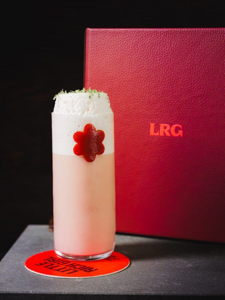 Cherry Lime Gin Fizz cocktail topped with foam and a flower garnish at Little Rich Girl in Flagstaff.