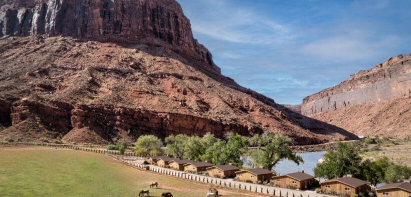Aerial view of Red Cliffs Lodge Moab with horses grazing in a pasture beside the Colorado River and towering red rock cliffs.