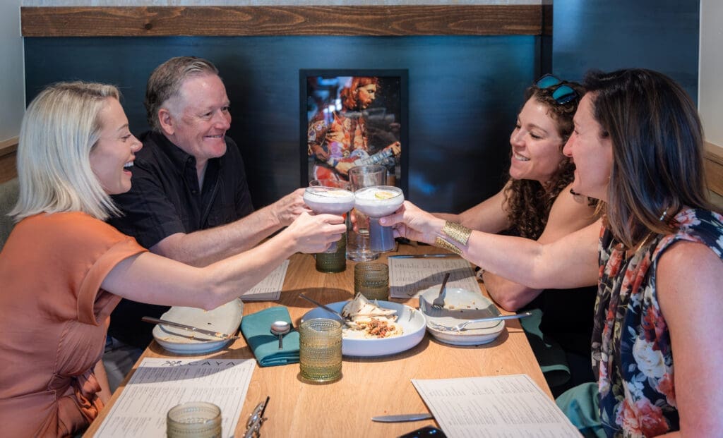 Friends cheers with handcrafted cocktails at a booth at CAYA restaurant in Edwards, Colorado.
